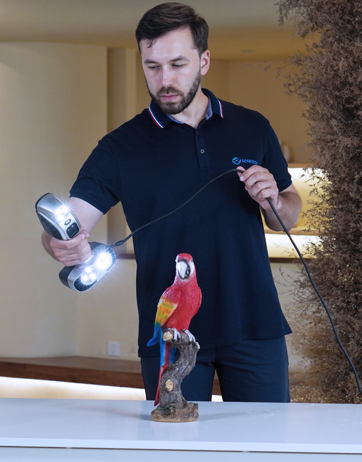 A man scanning a parrot statue with a 3D scanner on a white table.