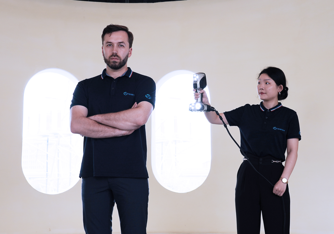 A man and woman standing with a 3D scanner in front of a white wall.